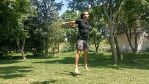 Persona haciendo jumping squats y saltando en un parque verde.